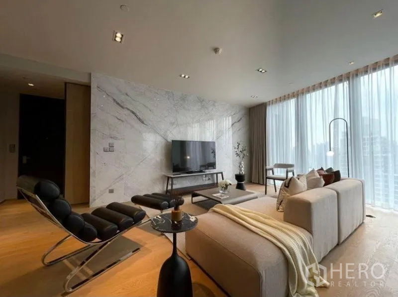 Condominium for rent or sale in Khlong Toei, Bangkok - Bright living room with marble feature wall, modern sofa set, and floor-to-ceiling windows with city views.