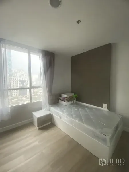 公寓 出租在Pathum Wan, Bangkok - 明亮卧室，落地大窗与城市景观，浅色木地板与单人床，位于巴吞旺公寓内。
