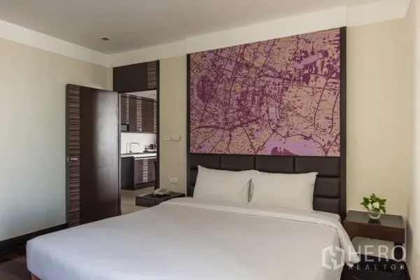 房间 出租在Khlong Toei, Bangkok - 主卧角度，可见紧凑厨房，软包床头与床头柜