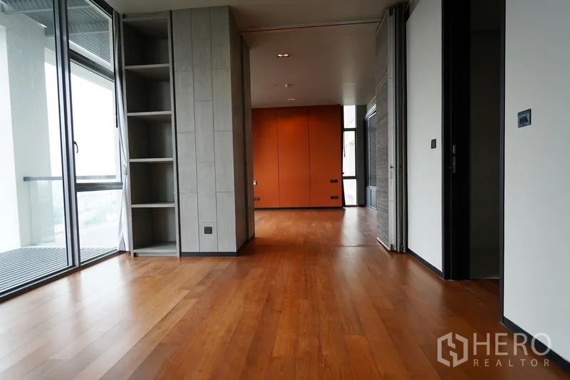 Condominium for rent in Sathon, Bangkok - Expansive suite with timber floors, shelving, sliding doors and access to a balcony.