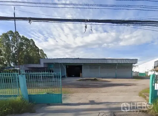 Warehouse for rent in Mueang Samut Sakhon, Samut Sakhon - Front façade of an industrial warehouse with gate and parking yard under blue sky.