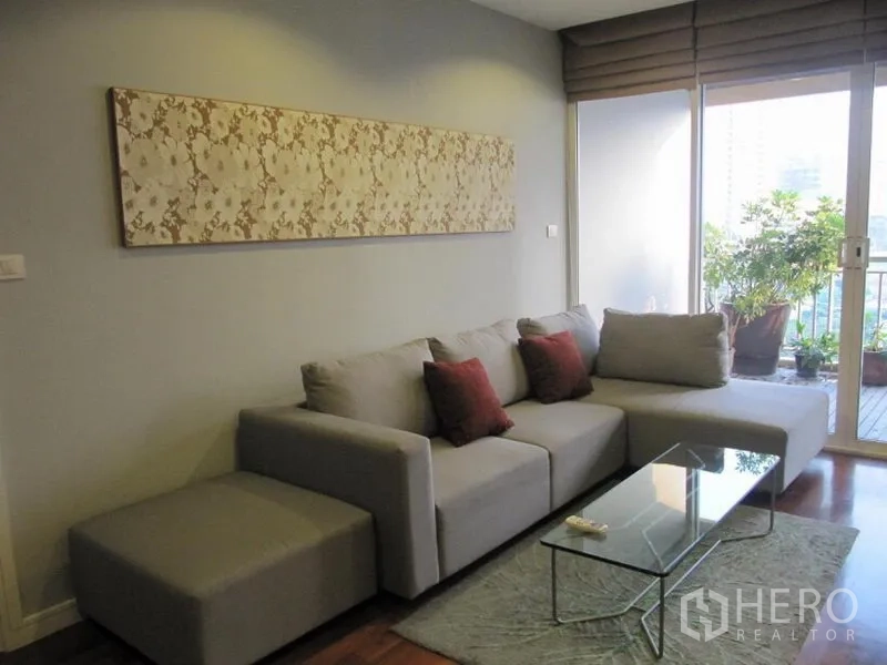 Condominium for rent in Khlong Toei, Bangkok - Cozy lounge featuring a gray sectional, red accent cushions, and a balcony with potted greenery.