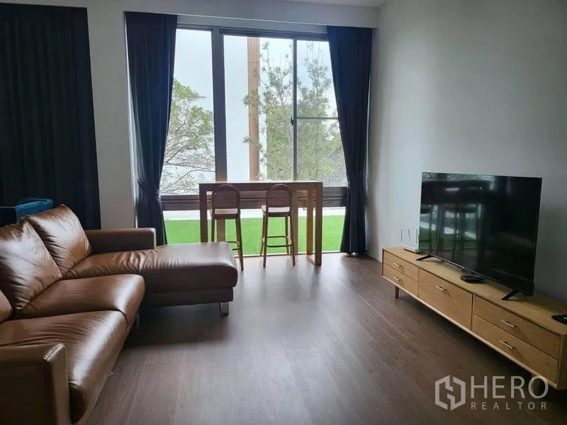 Detached House for rent in Saphan Sung, Bangkok - Bright living room with leather sectional, TV console and bar table by large windows opening to a green view.
