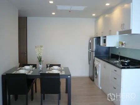 Condominium for rent in Watthana, Bangkok - Open-plan dining and kitchen with a table set, fridge, and built-in white cabinets.