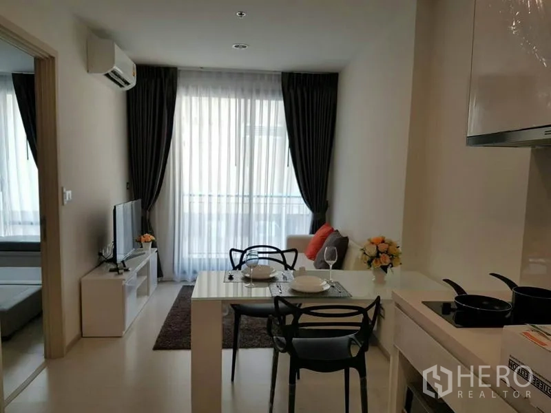 Condominium for rent in Khlong Toei, Bangkok - Bright living space with balcony access through sheer curtains and TV corner.