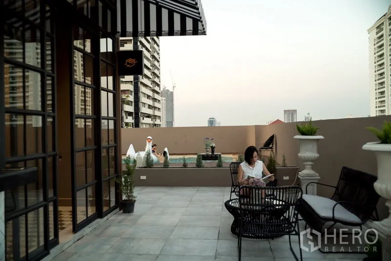Apartment for rent in Watthana, Bangkok - Rooftop terrace lounge with striped awning, outdoor seating and a view of the pool.