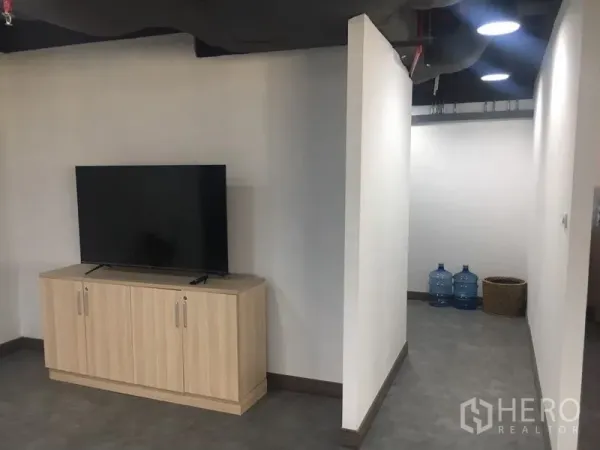 Office Space for rent in Sathon, Bangkok - Minimalist corridor with wood TV cabinet and storage, leading to utility area with water bottles.
