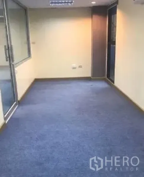 Office Space for rent in Bang Rak, Bangkok - Blue-carpeted office area with a glass partition door and ceiling lights.