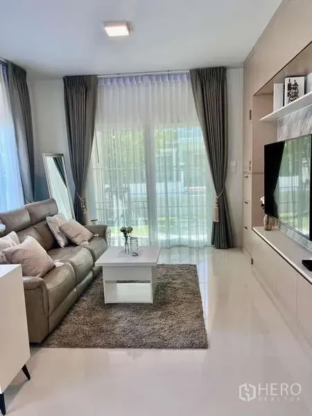 Detached House for rent in Bang Phli, Samut Prakan - Living room with sheer curtains, built-in TV wall and garden views.