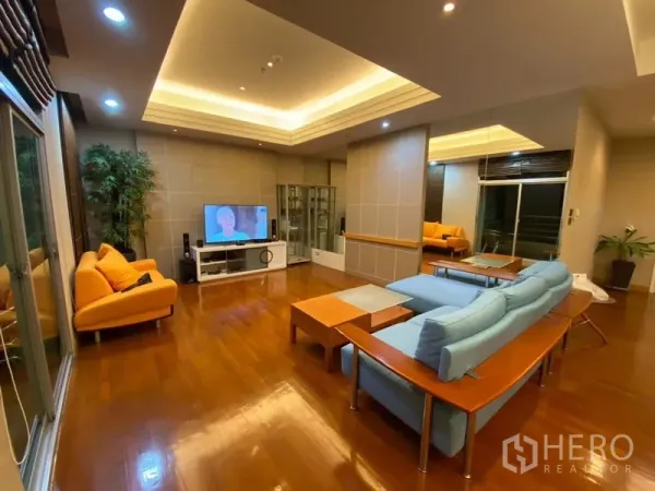 Condominium for rent in Pathum Wan, Bangkok - Spacious living room with recessed ceilings, wooden floors, TV and sliding doors to a balcony.