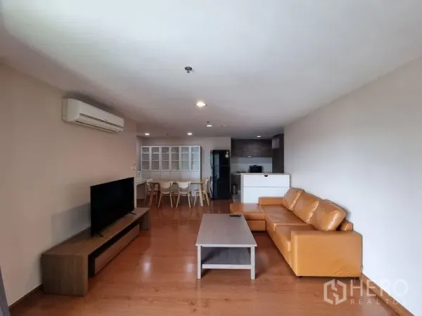 公寓 出租在Huai Khwang, Bangkok - 宽敞客厅，棕色皮沙发与电视柜，后方为开放式厨房。