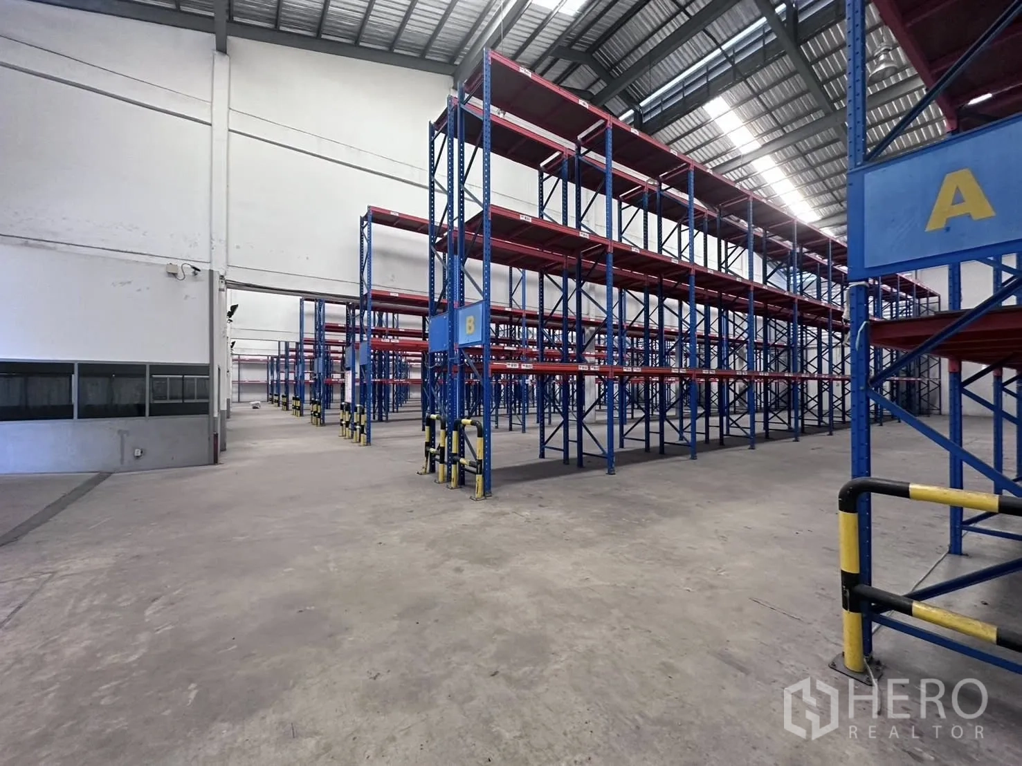Warehouse for rent in Mueang Samut Prakan, Samut Prakan - High‑ceiling warehouse interior with blue and red pallet racking systems installed.