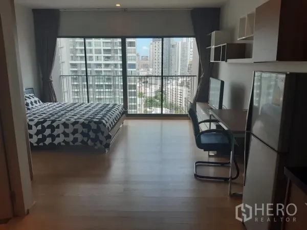 公寓 出租在Bangkok - 明亮的开间公寓，落地窗、床与书桌，阳台可望城市天际线。