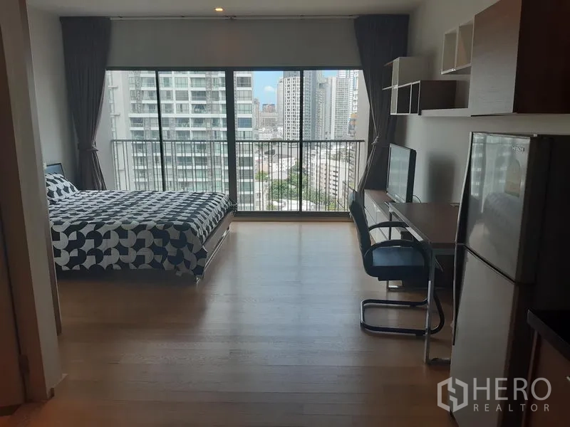 公寓 出租在Bangkok - 明亮的开间公寓，落地窗、床与书桌，阳台可望城市天际线。