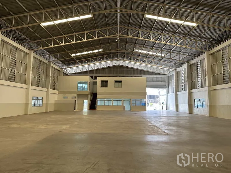 Factory for rent in Samut Prakan - Open warehouse hall with internal two-storey office block and wide roller doors for truck access.