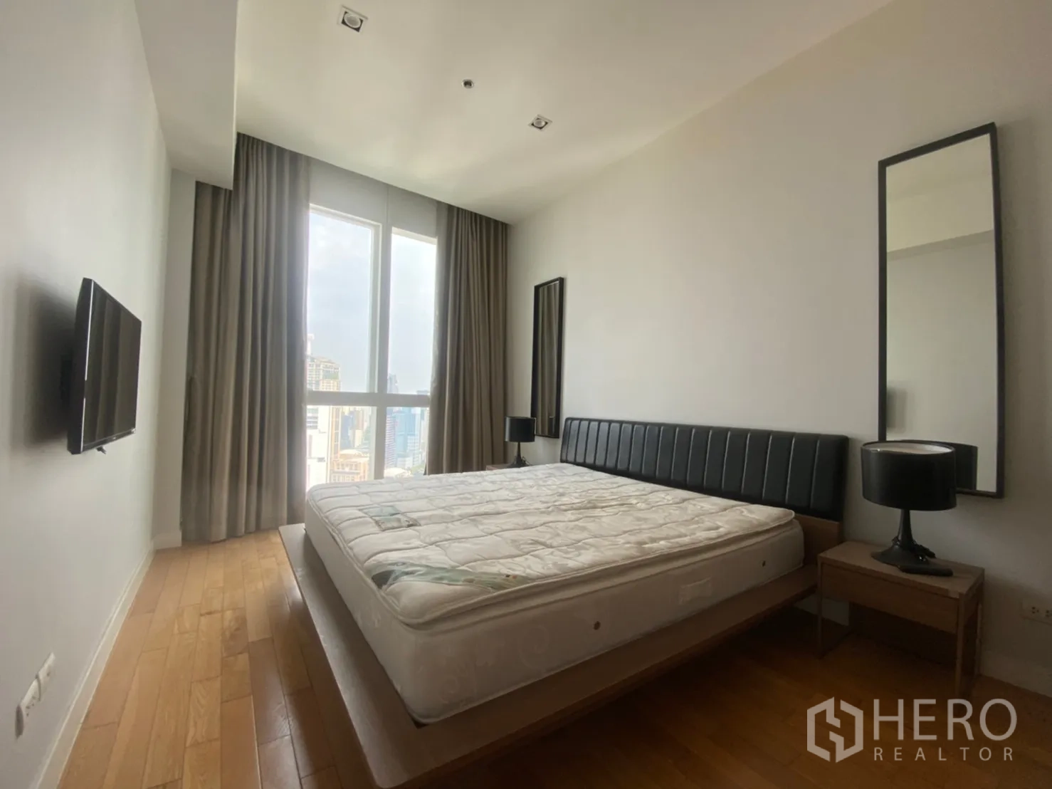 Condominium for rent or sale in Khlong Toei, Bangkok - Master bedroom with large window, city views, platform bed, bedside tables and wall-mounted TV.