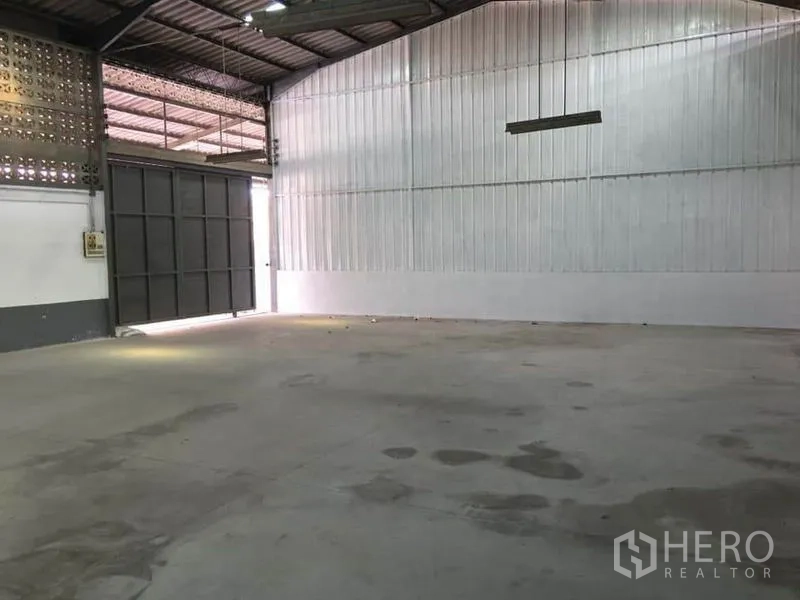 Warehouse for rent in Samut Prakan - Interior view toward a big sliding metal door and white corrugated wall.