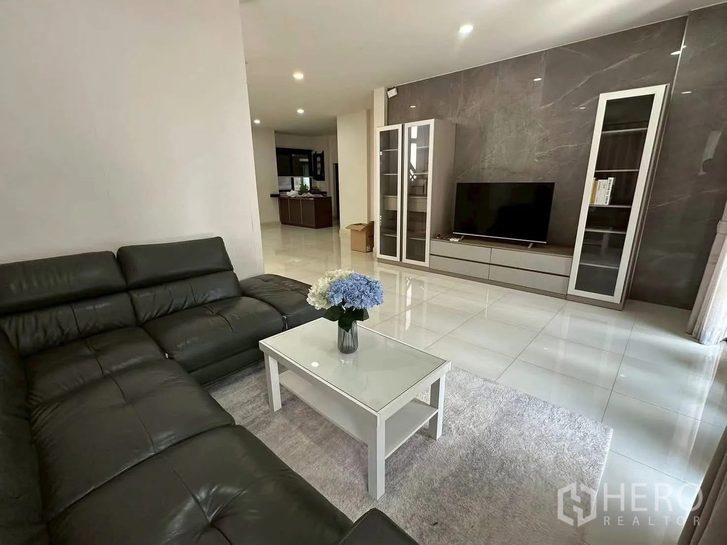 Detached House for rent in Bang Phli, Samut Prakan - Living area with sectional sofa facing a TV wall and glass display cabinets.