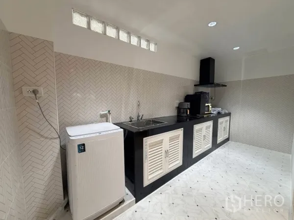 ทาวน์เฮาส์ for rent in Phra Khanong, Bangkok - ห้องครัวยาวผนังลายก้างปลา เคาน์เตอร์สีดำ อ่างล้างจาน เครื่องดูดควัน และเครื่องซักผ้า.