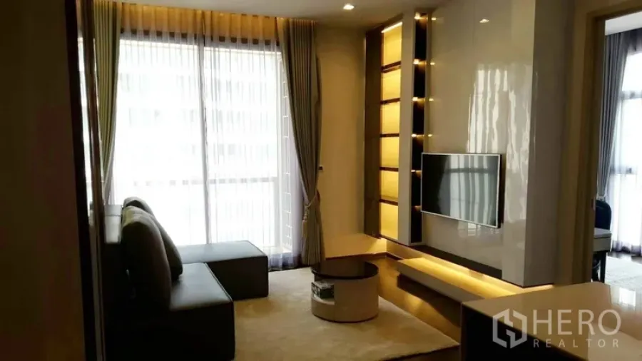 Condominium for rent in Watthana, Bangkok - Bright living room with floor-to-ceiling curtains, a TV wall and backlit shelves.