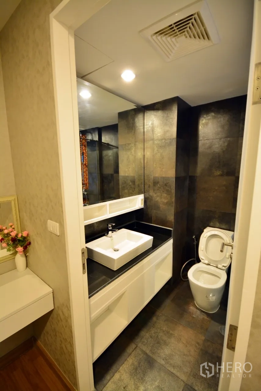 公寓 出租或出售在Watthana, Bangkok - 现代浴室，深色石材墙面，玻璃淋浴间，白色台盆柜与坐便。