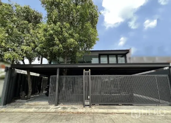 独立式住宅 出租或出售在Phra Khanong, Bangkok - 曼谷Phra Khanong现代独栋房屋外观，高大绿树与黑色金属围栏。