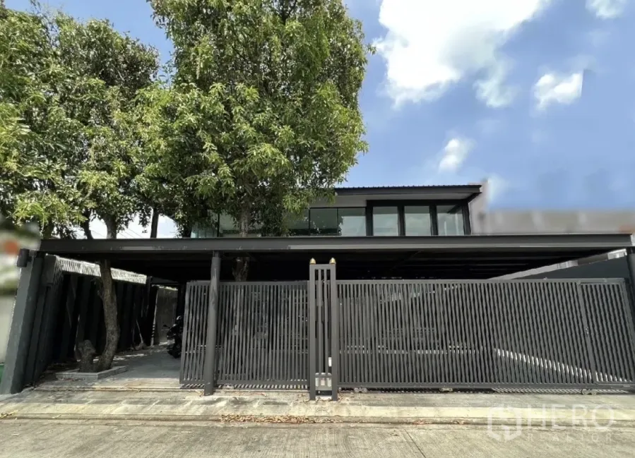 Detached House for rent or sale in Phra Khanong, Bangkok - Modern detached house exterior in Phra Khanong, Bangkok with tall tree, black metal gate and upper-floor windows.