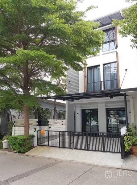 Townhouse for rent in Suan Luang, Bangkok - Three-storey modern townhouse facade in Suan Luang with gated carport and a large shade tree.