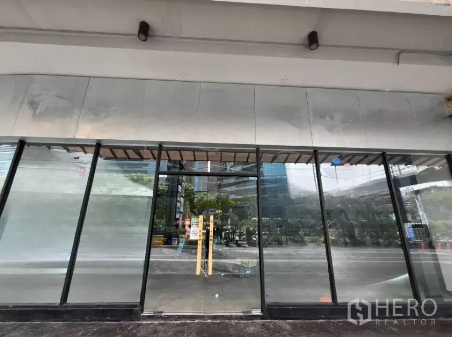 零售空间 出租 - 临街店面外立面，整面落地玻璃与双开门，雨棚下映出城市景观。
