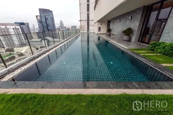 公寓 出租在Watthana, Bangkok - 高楼层长泳池，玻璃护栏与城市景观，旁设绿化平台。