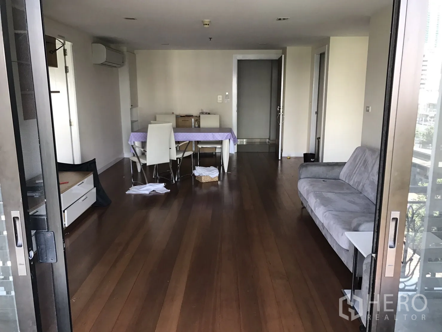 公寓 出租或出售在Watthana, Bangkok - 从阳台望入的开放式客厅，木地板、灰色沙发与餐桌。