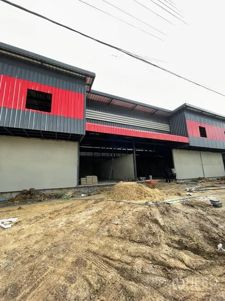 货栈 出租在Pathum Thani - 一排相连的仓库单元，红色装饰带，前场仍在整地。