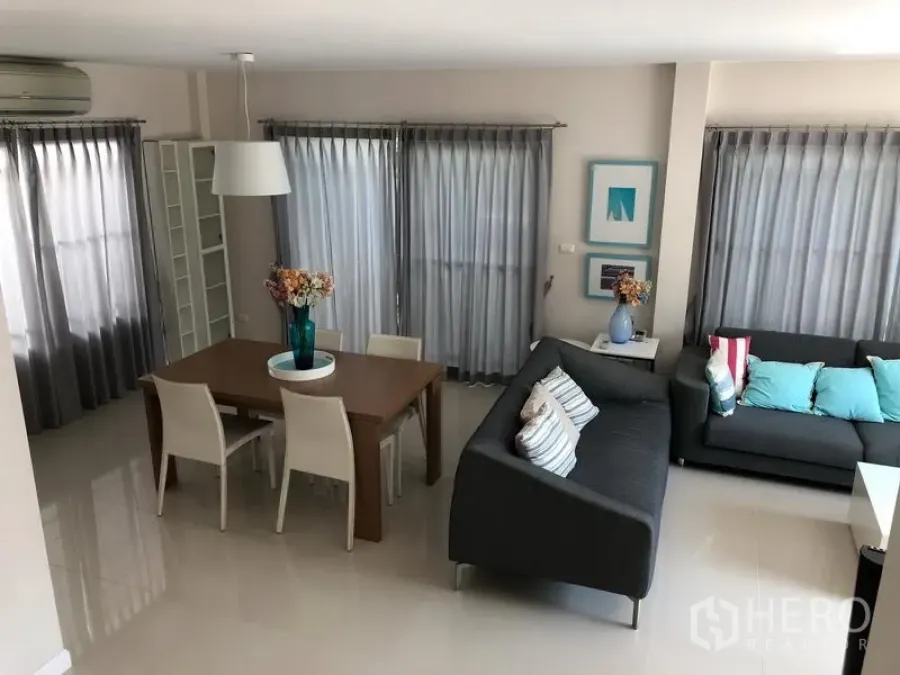 Detached House for rent in Bang Kapi, Bangkok - Aerial view of the living–dining space featuring grey sofas, a wooden table and full-height curtains.