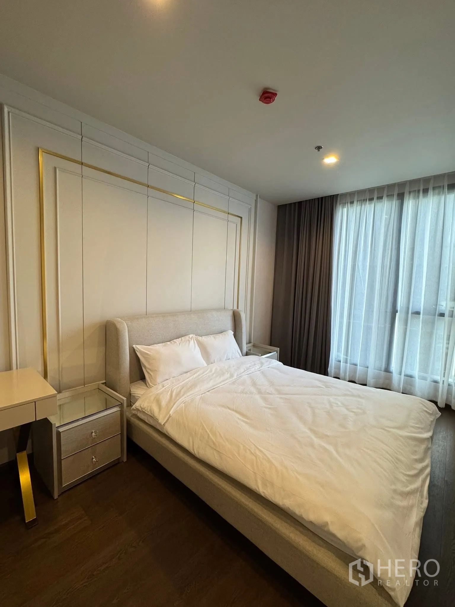 Condominium for rent in Khlong Toei, Bangkok - Bright bedroom with upholstered bed, side tables and sheer curtains.