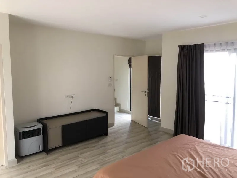 Townhouse for rent in Saphan Sung, Bangkok - Master bedroom corner showing balcony curtains and doorway to staircase
