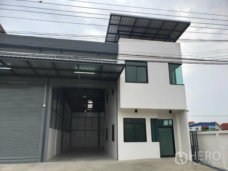 Warehouse for rent or sale in Lam Luk Ka, Pathum Thani - Modern warehouse exterior with two-storey office block, large roller shutter and metal awning in Lam Luk Ka.