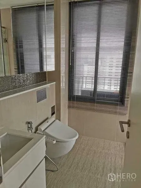 Condominium for rent or sale in Phra Khanong, Bangkok - Second bathroom with window blinds, wall-mounted bidet toilet and compact vanity.