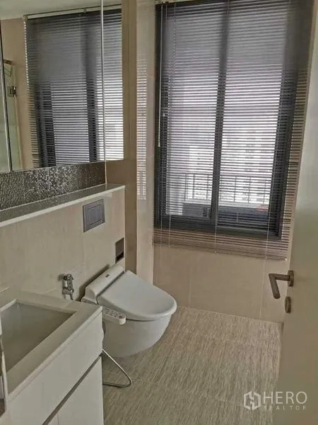 Condominium for rent or sale in Phra Khanong, Bangkok - Second bathroom with window blinds, wall-mounted bidet toilet and compact vanity.