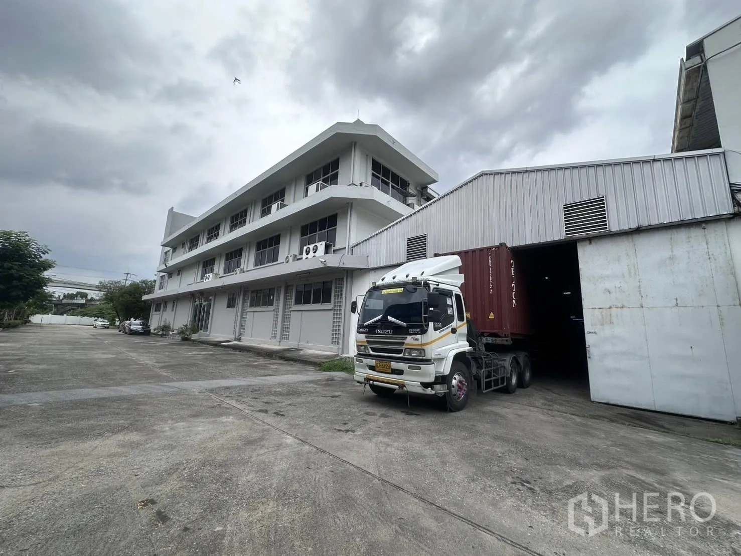 Warehouse for rent in Mueang Samut Prakan, Samut Prakan - Container truck positioned at a warehouse bay beside the office block under an overcast sky.