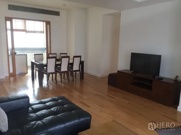 Condominium for rent in Khlong Toei, Bangkok - View from living to dining with sliding door to the closed kitchen and a wooden TV cabinet on hardwood floors.