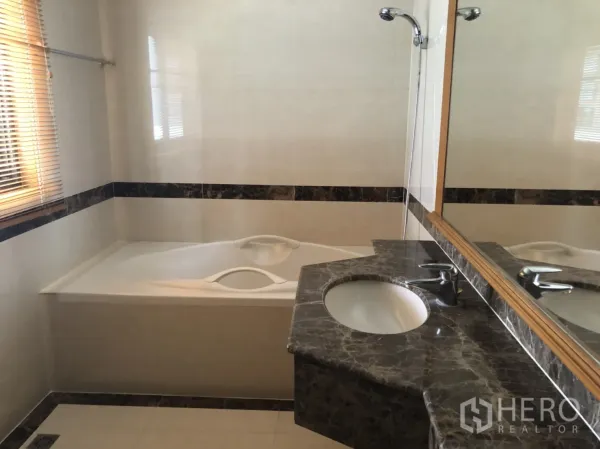 Apartment for rent in Bang Rak, Bangkok - Bathroom featuring soaking bathtub, large mirror and marble countertop vanity with sink.