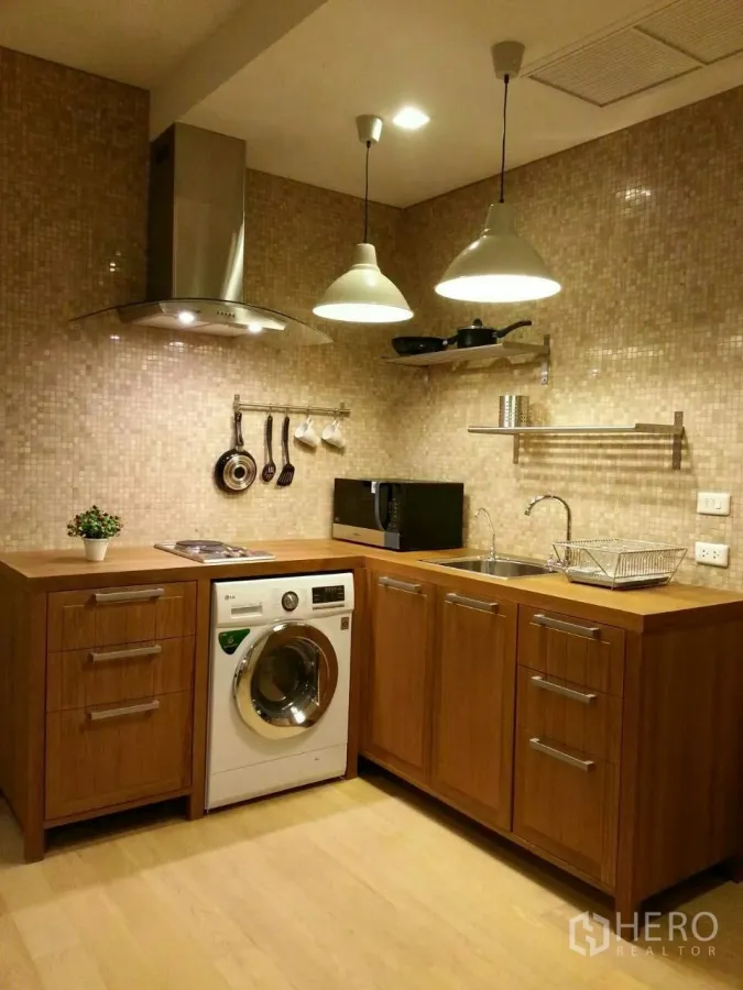 Condominium for rent or sale in Watthana, Bangkok - Modern Ekkamai condo kitchenette with wood cabinets, washing machine, cooktop, hood and pendant lights.