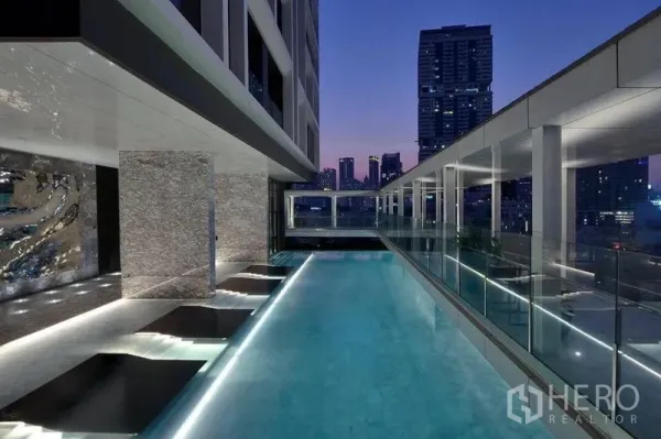 Condominium for rent in Khlong Toei, Bangkok - Rooftop infinity pool with city skyline views and sunken loungers at dusk.