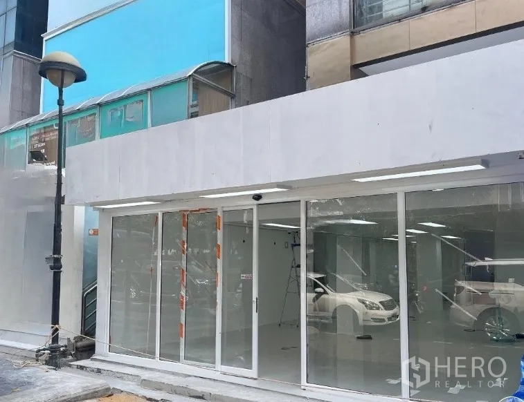 Retail Space for rent in Khlong Toei, Bangkok - Street-front retail shop with floor-to-ceiling glass and sliding doors at the base of a mid-rise building.