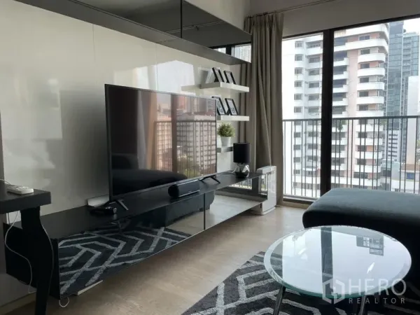 Condominium for rent in Bangkok - Media wall with large flat-screen TV, glass coffee table and balcony access.