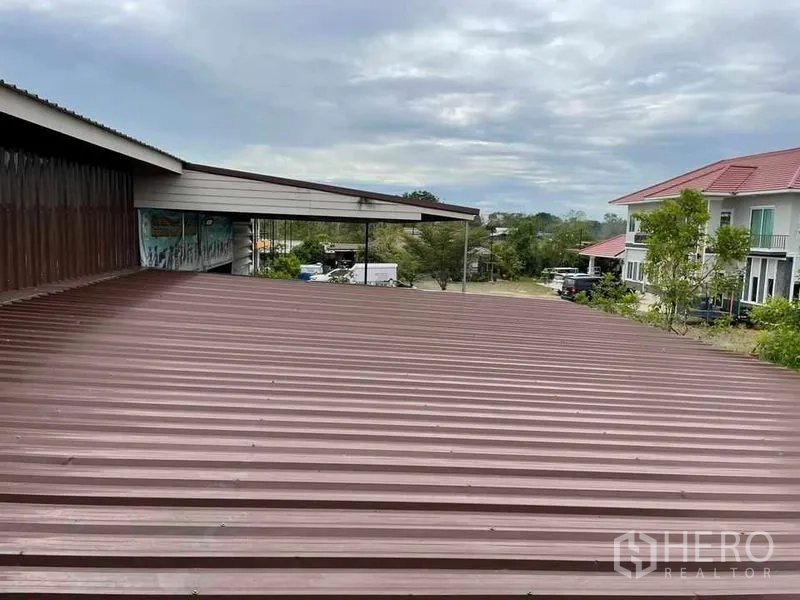 Warehouse for rent or sale in Pathum Thani - Close view of corrugated metal warehouse roof with nearby homes in the background.