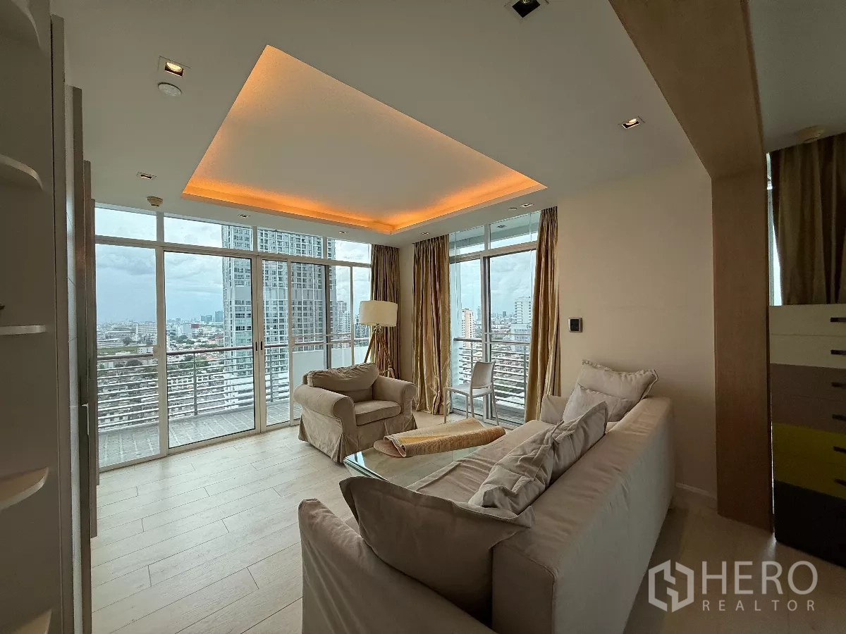 Condominium for rent in Phaya Thai, Bangkok - Bright lounge with recessed lighting, beige sofas and wide glass walls opening to a balcony and skyline view.