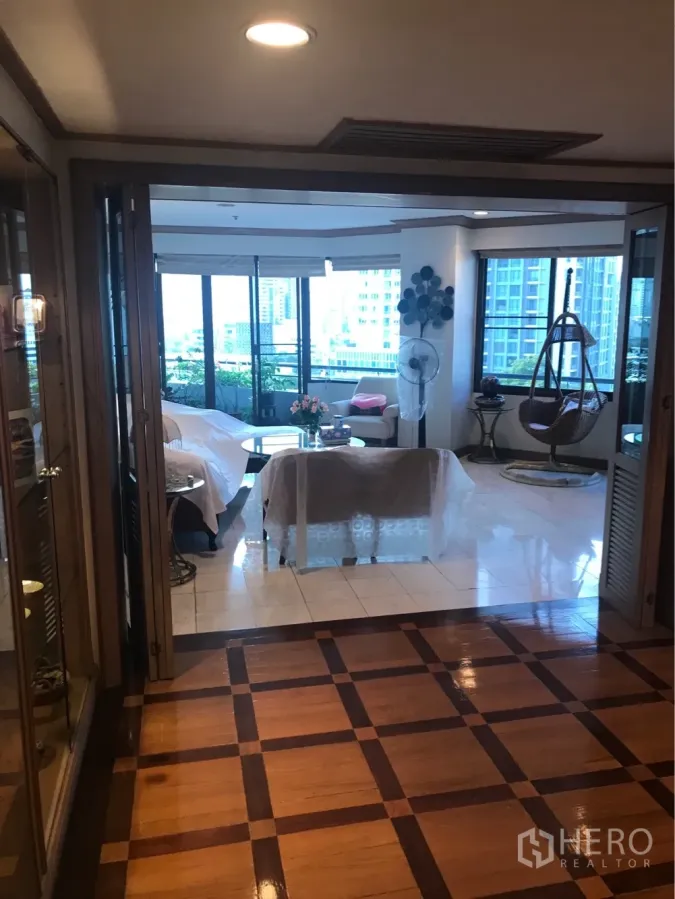 Condominium for rent or sale in Watthana, Bangkok - Foyer with patterned wooden flooring opening to a bright living room with large windows and balcony greenery in a Bangkok condo.
