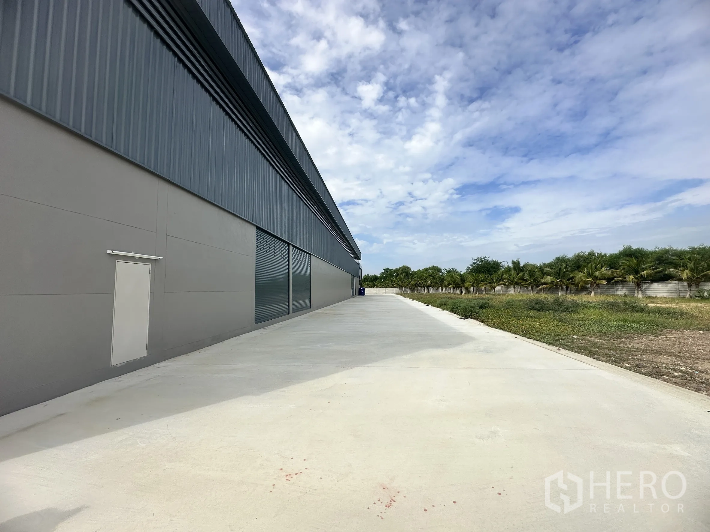 工厂 for rent or sale in Bang Len, Nakhon Pathom - 仓库侧立面，设有卷帘门、金属墙板和人员门，连接宽阔通道。