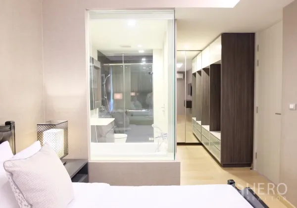 Condominium for rent in Watthana, Bangkok - Ensuite layout showing glass-walled bathroom with tub and long wardrobe corridor from the bedroom.